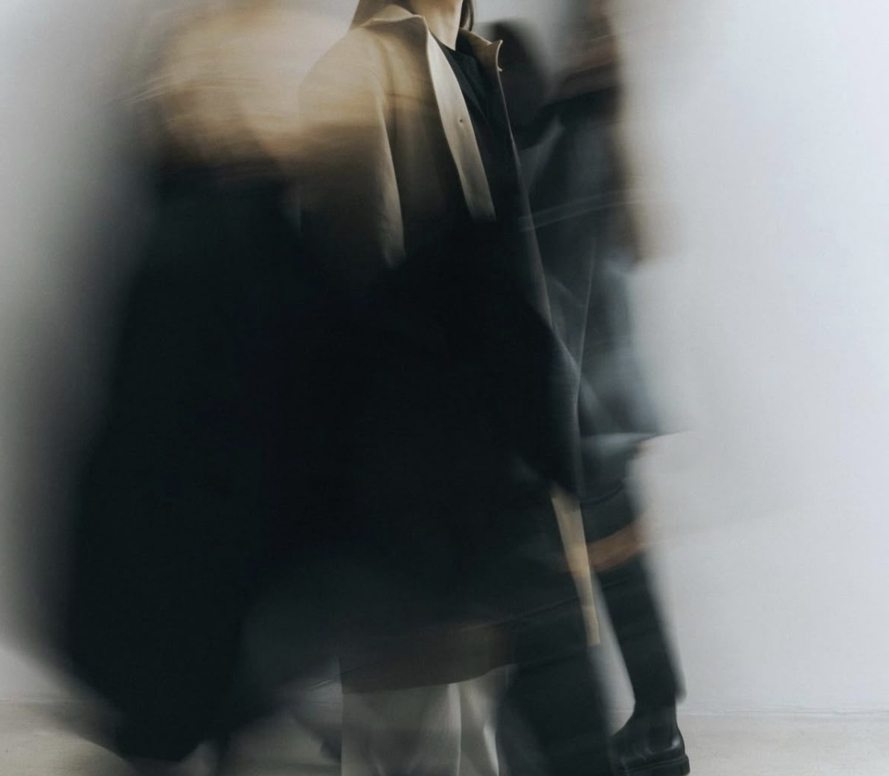 Blurred motion of people walking indoors against a plain white wall.
